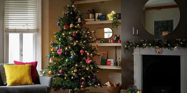 HAB 7ft green mixed tip natural upswept Christmas tree next to a window decorated with multicoloured baubles. 